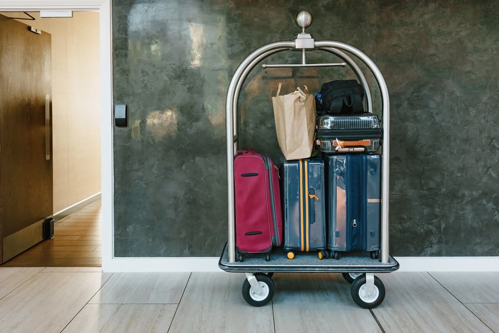 Hotel luggage trolley loaded with colorful suitcases and travel bags standing in hallway near room entrance, Hospitality service